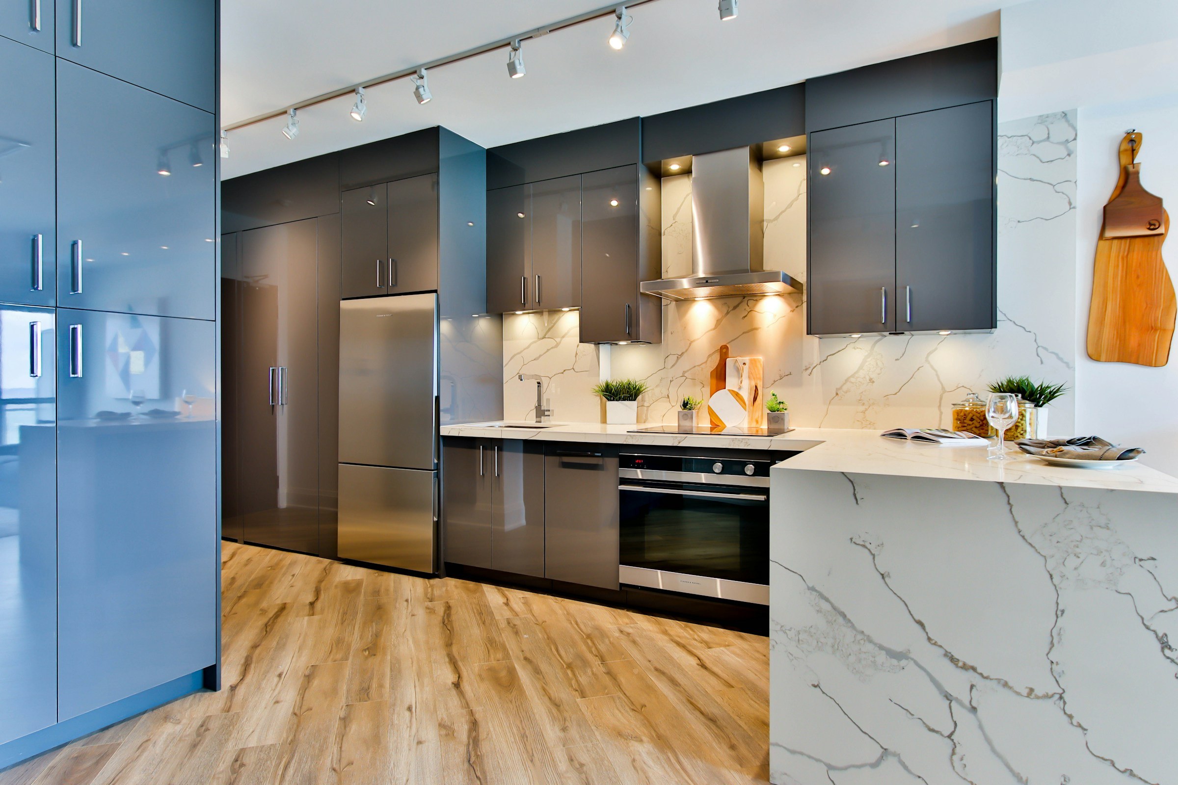 Modular kitchen combining gloss blue tall units, dark cabinets and a marble waterfall counter